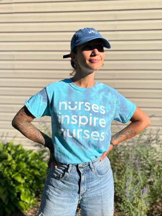 Person wearing a blue 'nurses inspire nurses' t-shirt and cap outdoors.